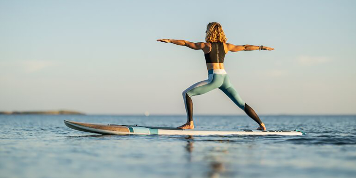 An athletic woman in a warrior 2 yoga stance on a stand-up paddleboard.